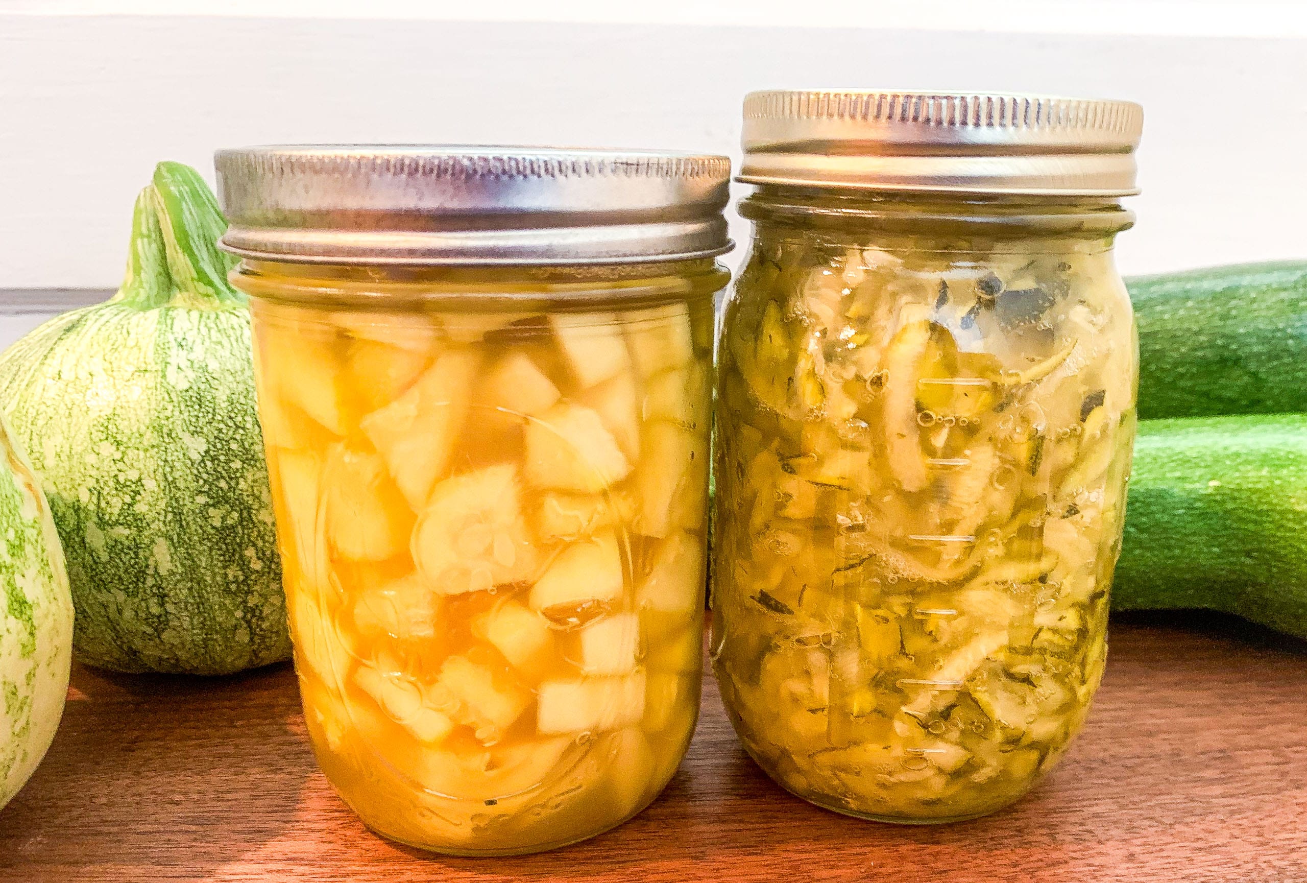 two mason jars of pineapple with zucchini behind the jars on a wood counter