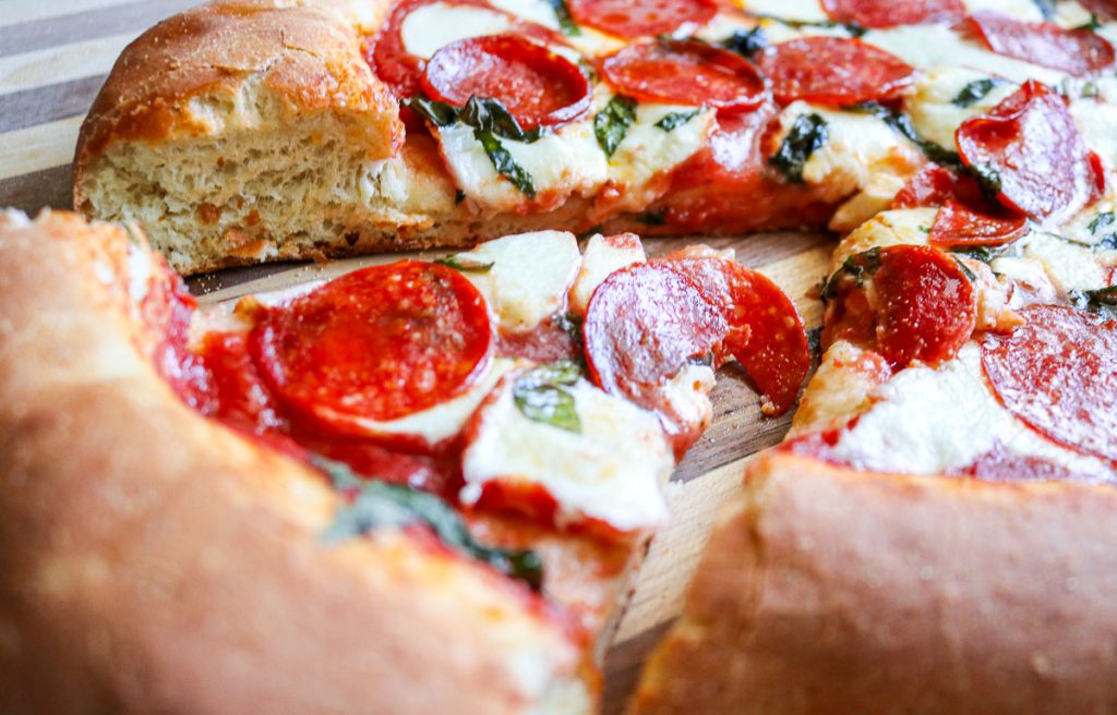 a piece of sourdough pizza being pulled out from the pie