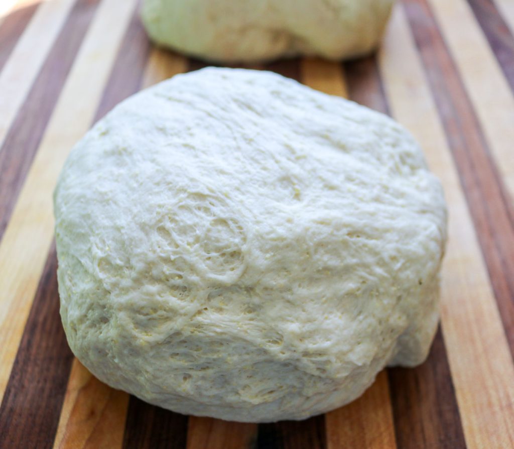 two sourdough pizza dough balls on a wooden cutting board