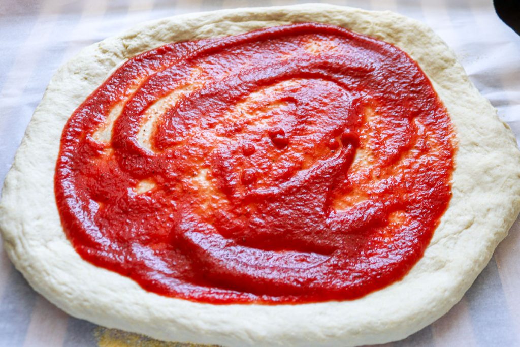 pizza sauce spread on a sourdough pizza crust