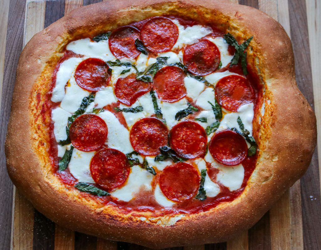 whole sourdough pepperoni pizza on a wooden cutting board