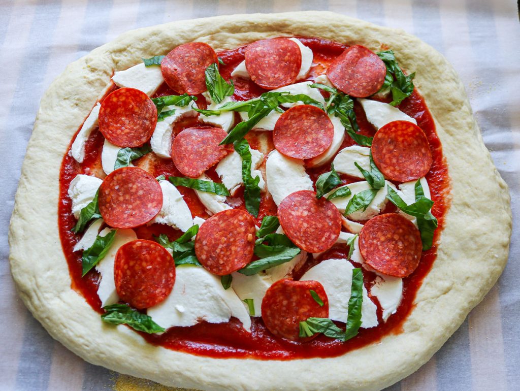 unbaked whole sourdough pepperoni pizza on parchment paper