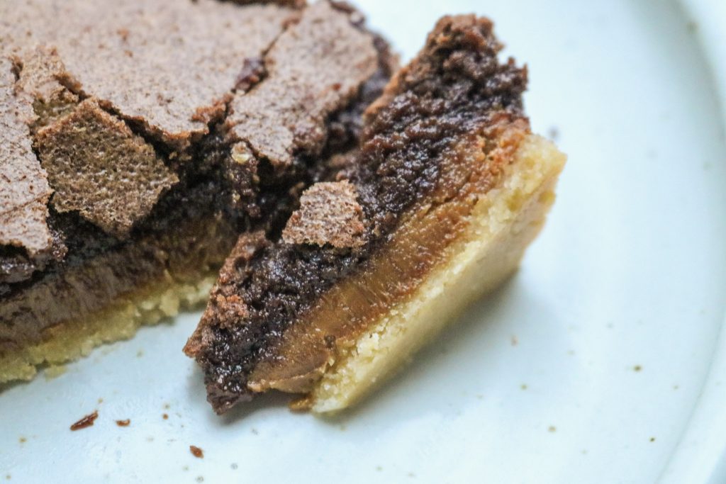 sliced chocolate caramel bar turned on its side to show the layers on top of a white plate