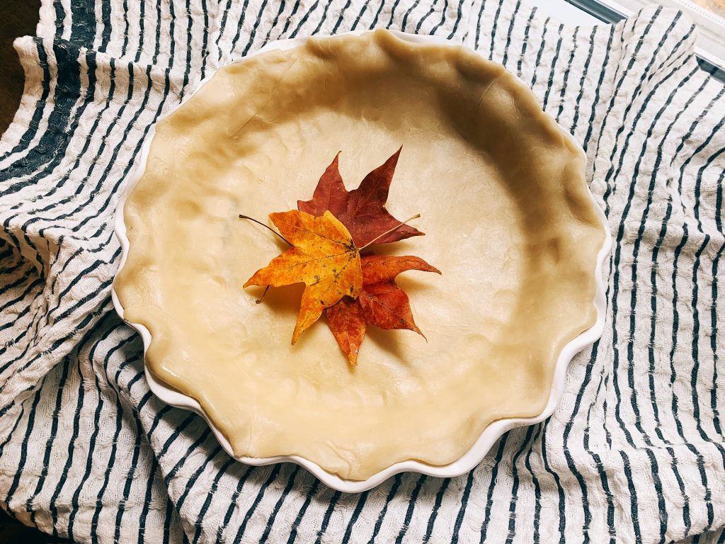 Pie crust on a white and black striped towel with leaves in the center of the crust