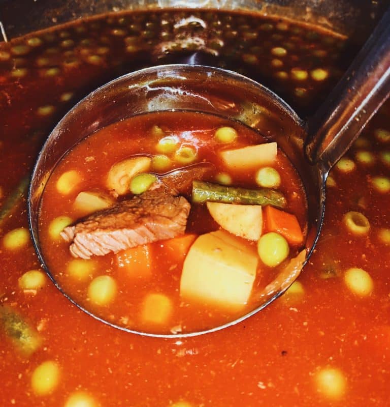 ladle in a pot of vegetable soup with prime rib pieces