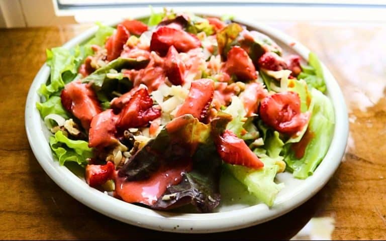 lettuce, strawberries, cheese on white plate with strawberry dressing