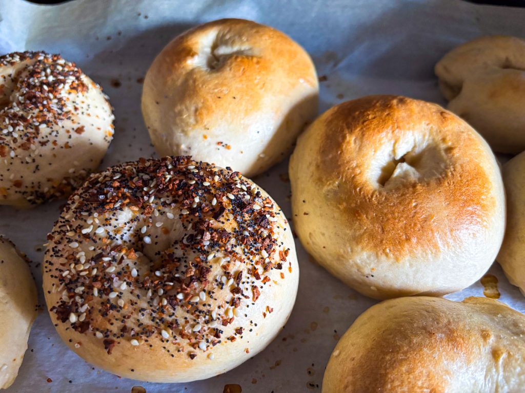 Everything-seasoned sourdough bagels cooling on parchment paper.