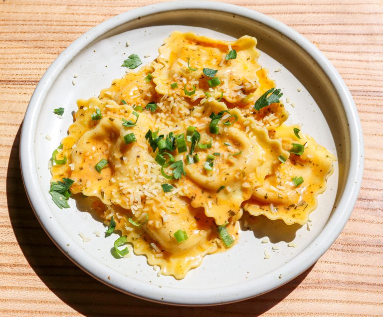 a white plate of lobster ravioli with butter sauce, chives and parmesan