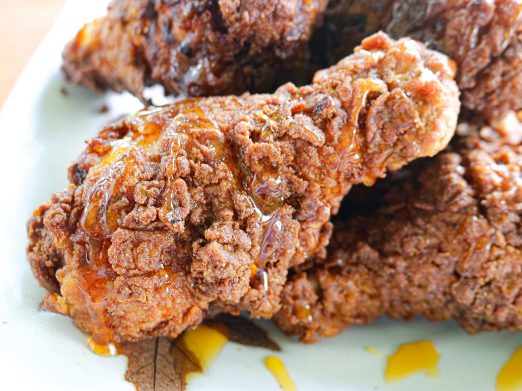 a plate of fried chicken with hot honey drizzled on top a drumstick