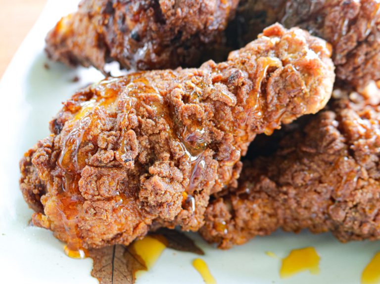 a plate of fried chicken with hot honey drizzled on top a drumstick