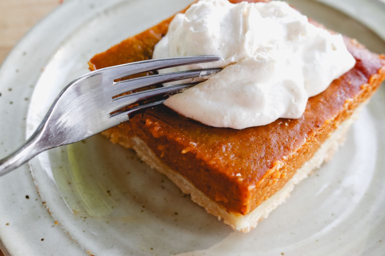 pumpkin pie bar with whipped cream being cut into by a fork on a white plate