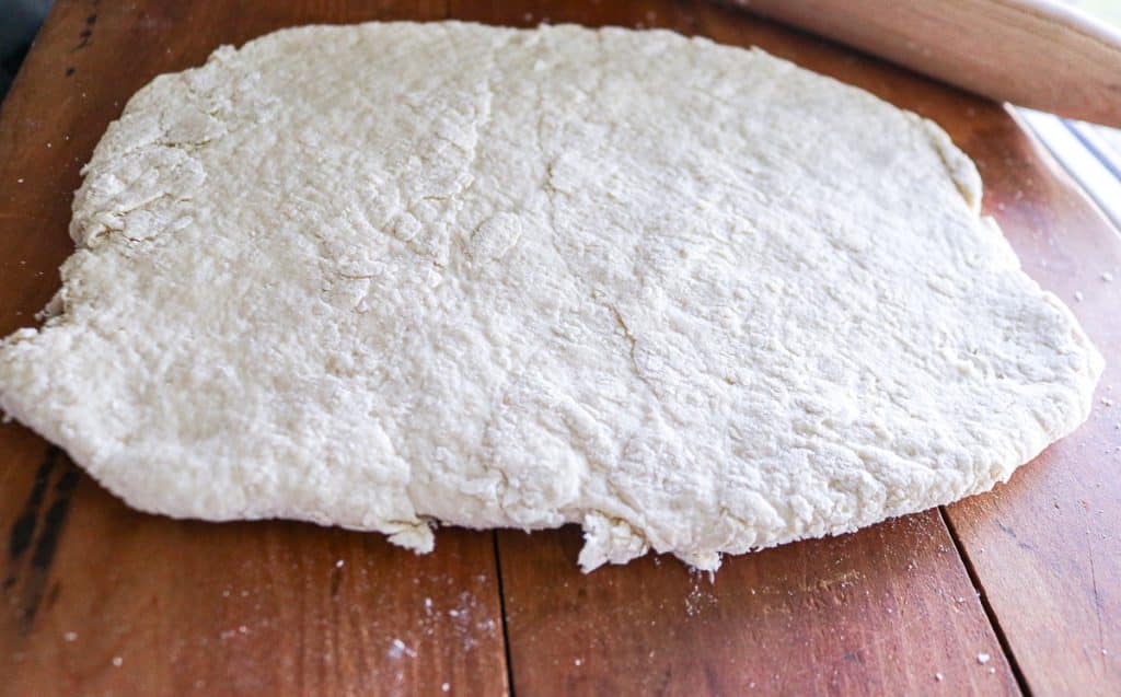 Rolled-out sourdough biscuit dough on a floured wooden surface before cutting.