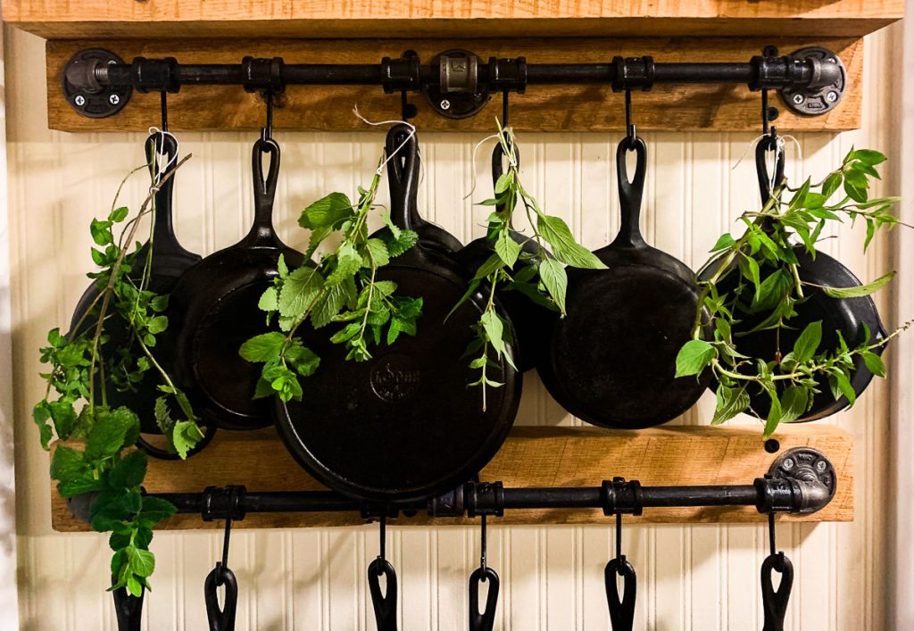 cast iron skillets hanging from a wooden rack with herbs hanging between them to dry