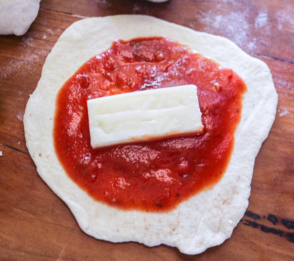 one slice of dough rolled out in a circle and topped with marinara and mozzarella