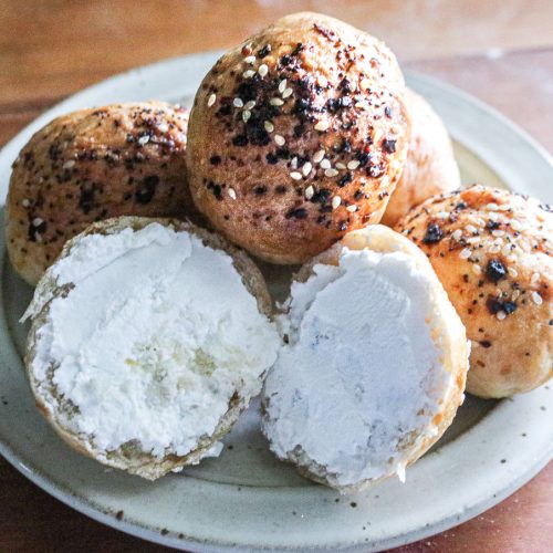 stack of miniature bagels on a plate with one cut in half and spread with cream cheese