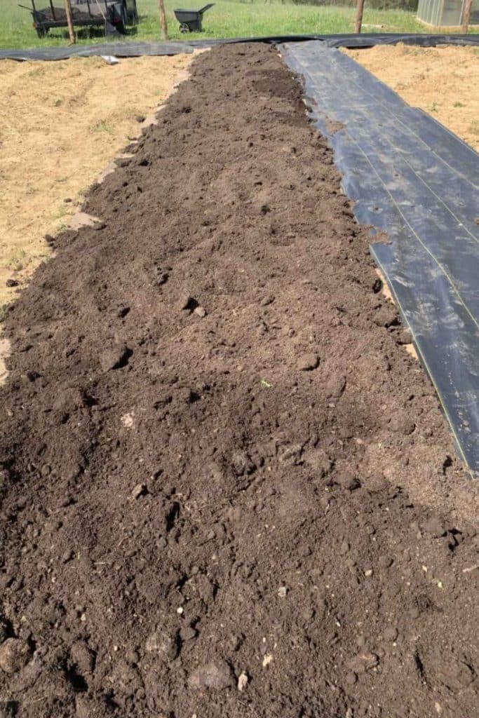 prepared soil in a garden bed with a plastic fabric walkway