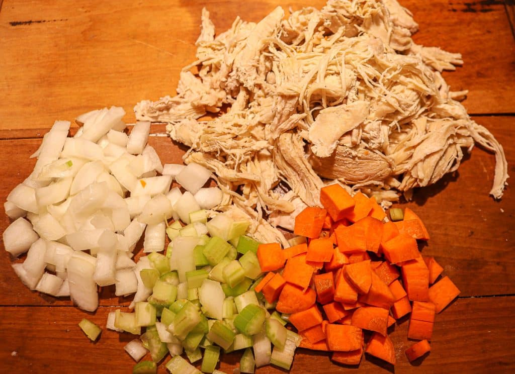 cut carrots, celery, onion and shredded chicken on a wooden cutting board