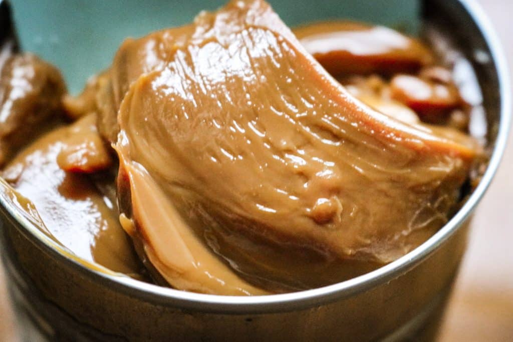 eagle brand caramel being dipped out of a can with a blue silicon spatula