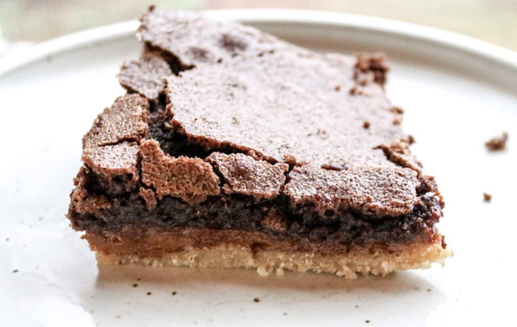 cut piece of a chocolate caramel shortbread bar on a white plate