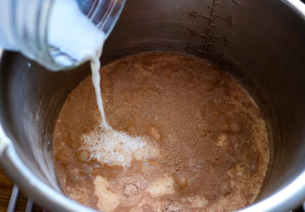 milk being poured into a stainless pan of chocolate pudding mix