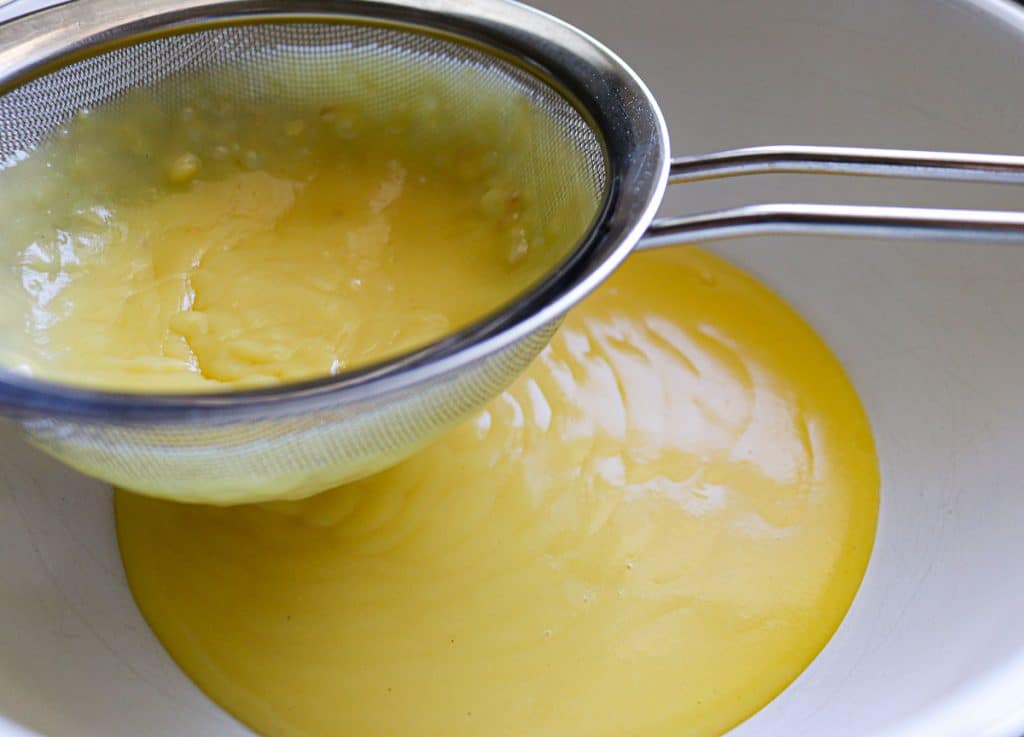 vanilla pudding going through a mesh sieve into a white bowl