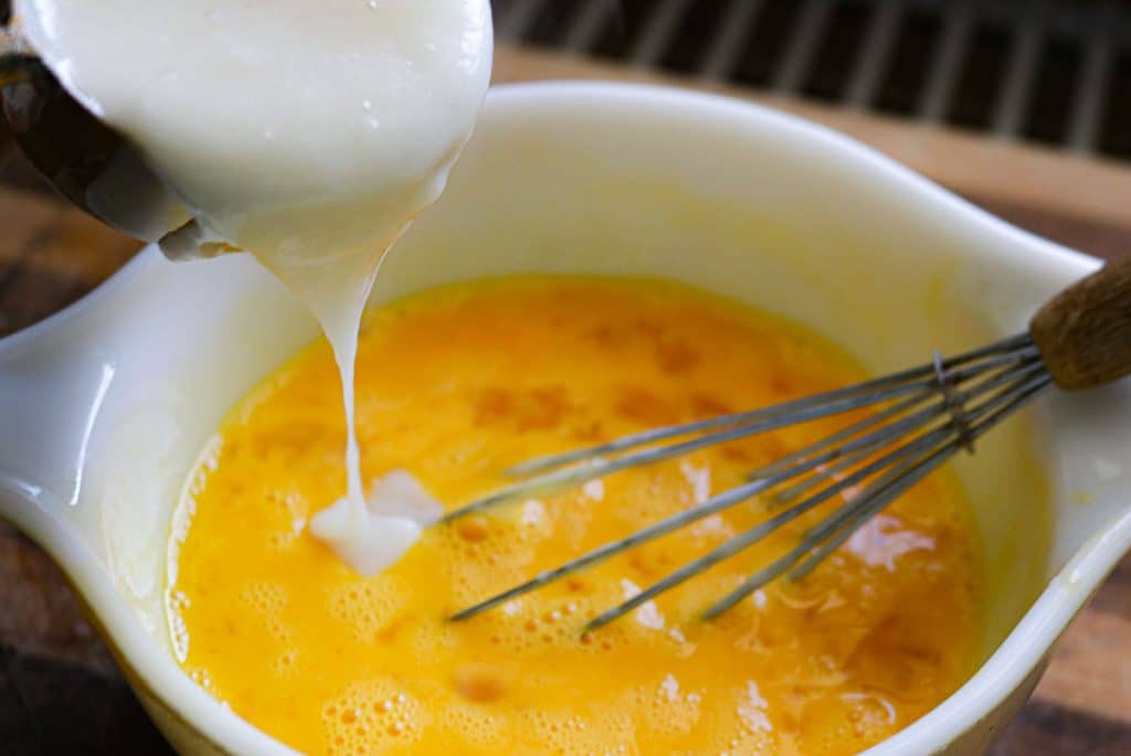 pouring vanilla pudding base into a bowl of eggs with a whisk