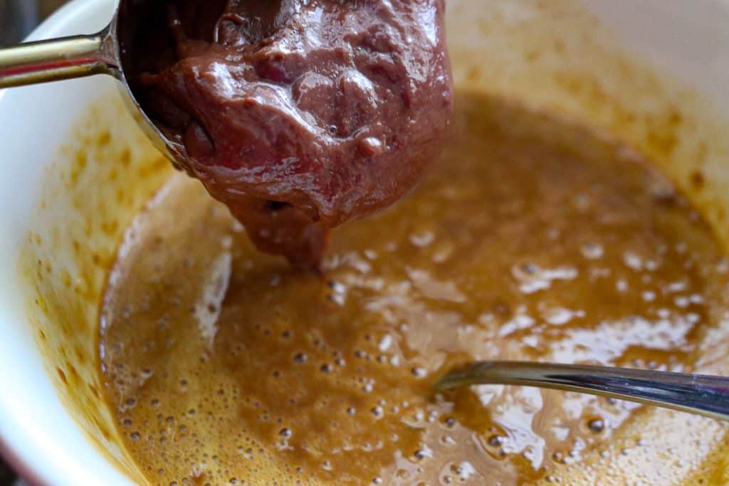 a fork whisking hot chocolate pudding into a white bowl filled with eggs