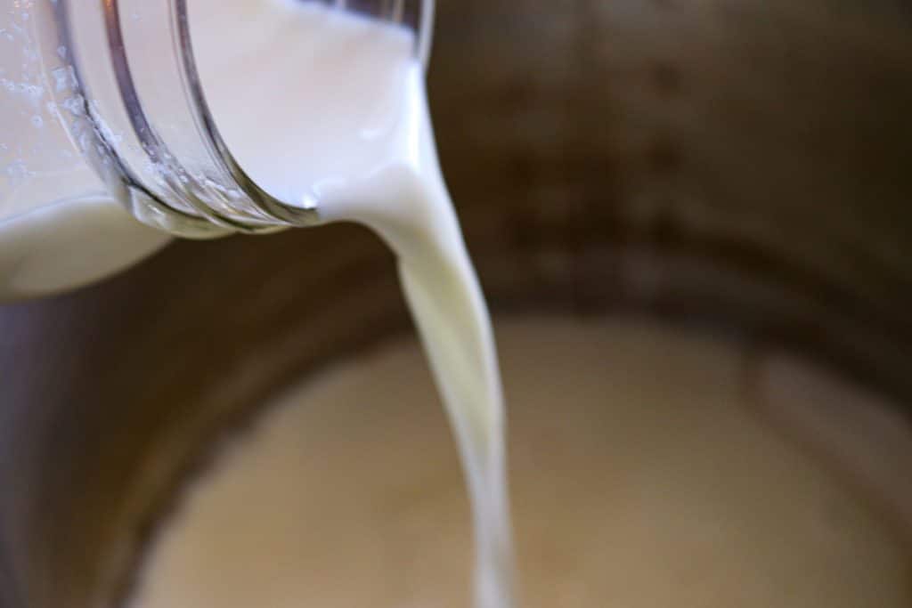 pouring milk in a glass jar onto vanilla pudding mix