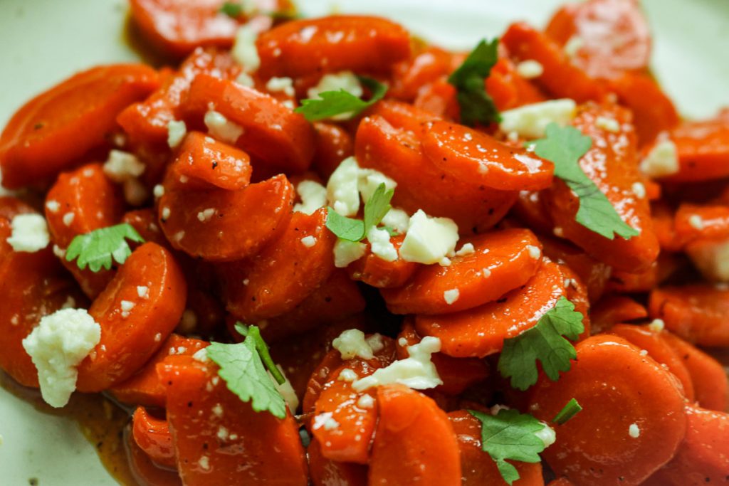 Hot honey carrots served on a plate with feta crumbles and chopped cilantro.
