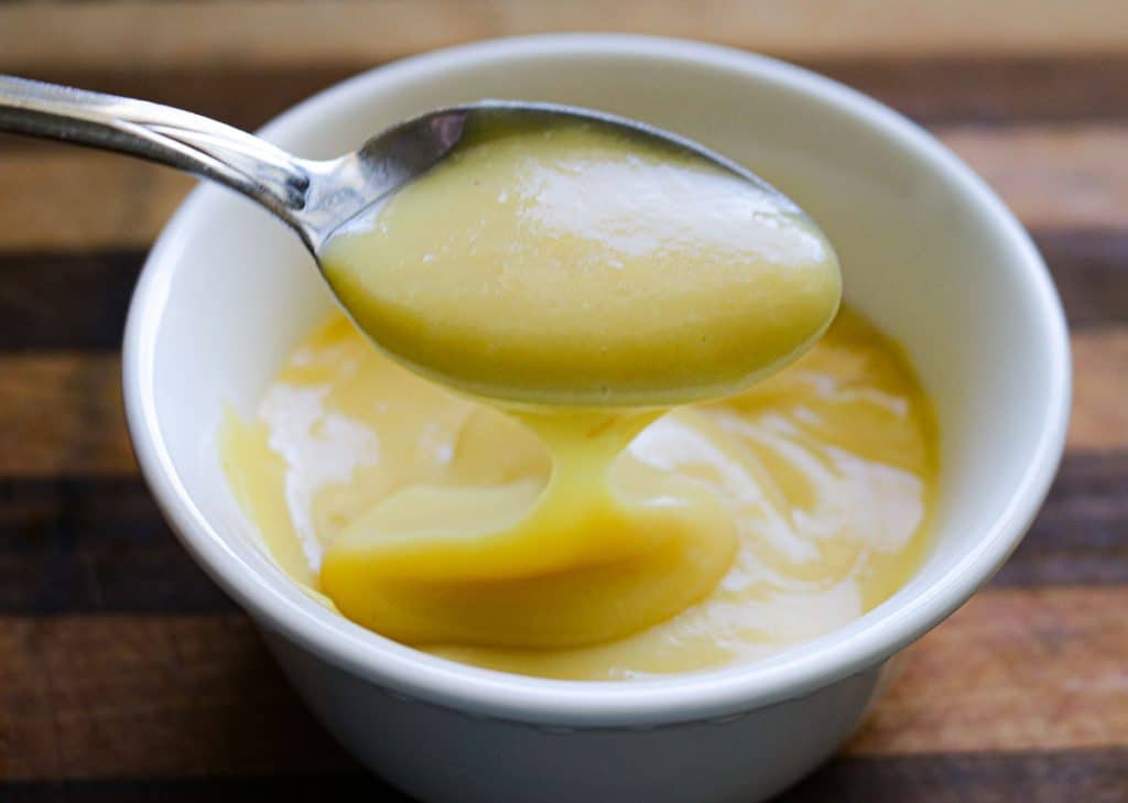 spoonful of vanilla pudding over a white bowl of vanilla pudding on a wooden counter