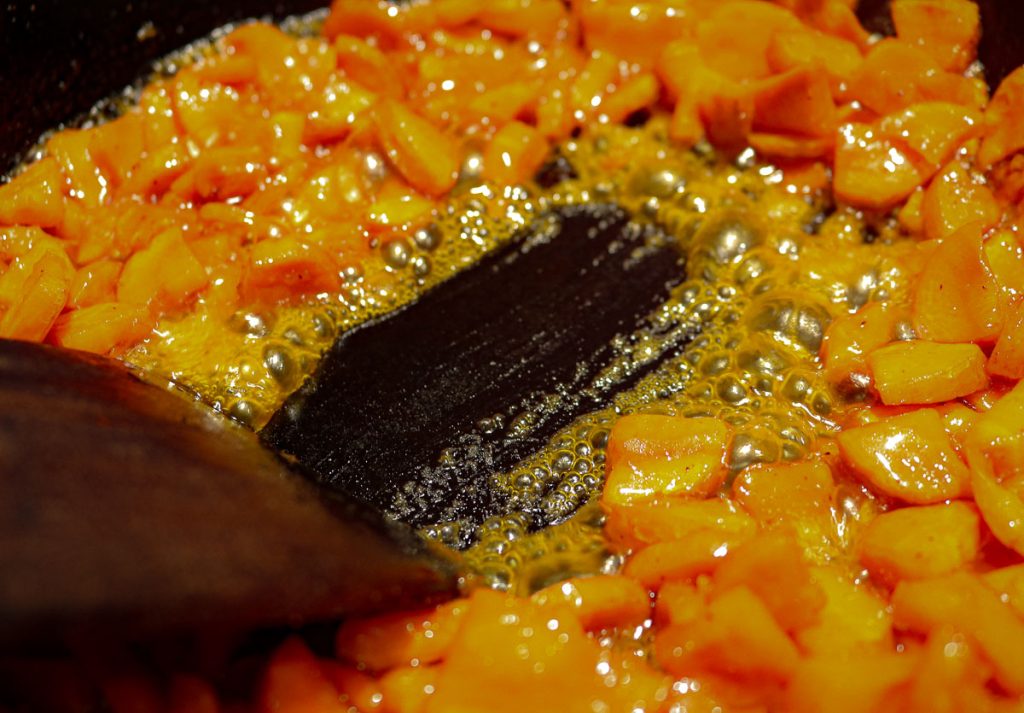 spatula dragging through a carrots in a honey glaze in a cast iron pan