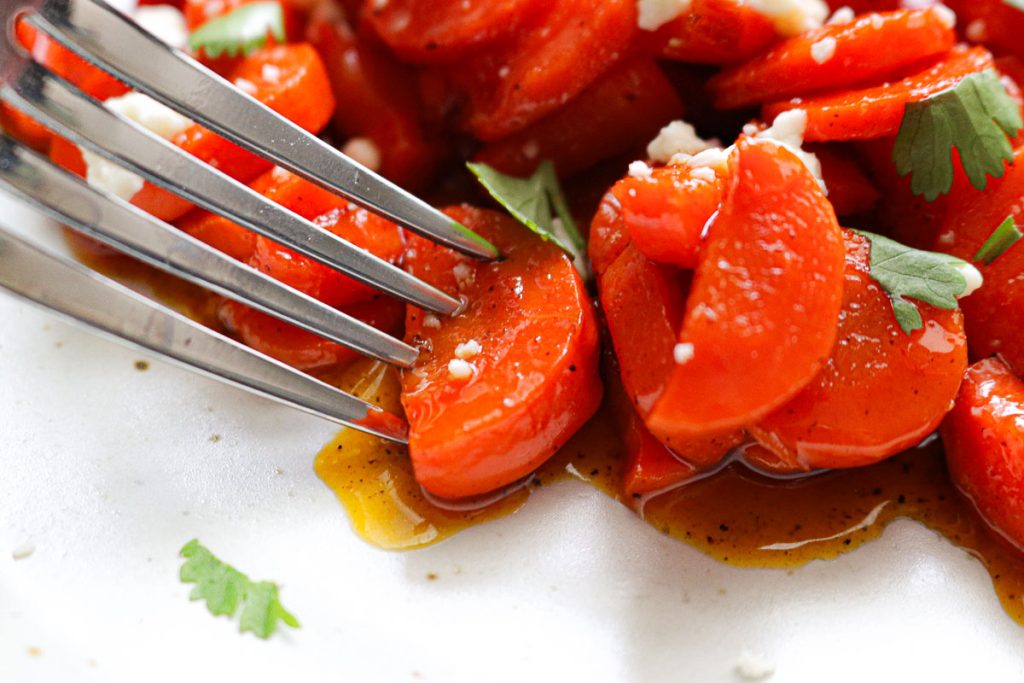 a fork piercing a carrot on a white plate