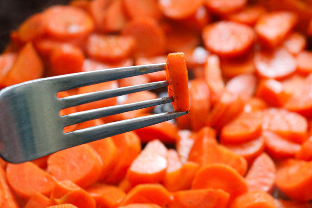 a fork piercing a sliced carrot over a pan of carrots