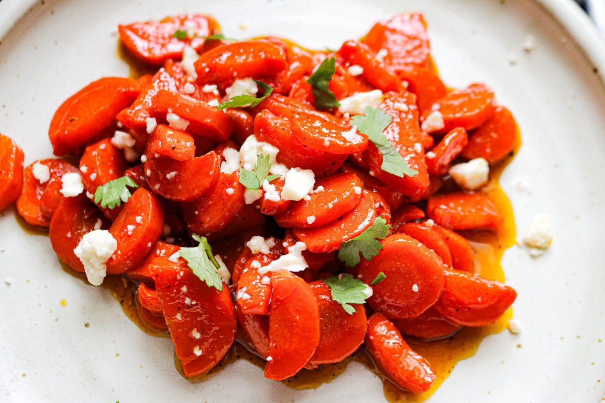 a white plate of sliced glazed carrots with feta and herbs