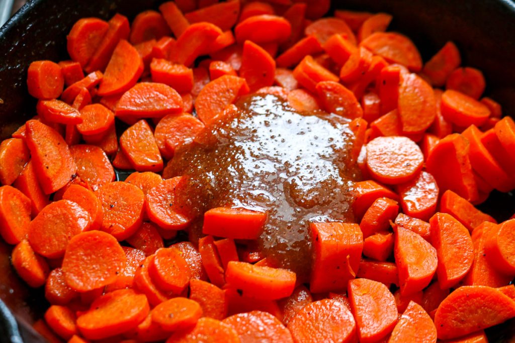 sliced carrots in a cast iron pan with a honey mixture dolloped in the middle