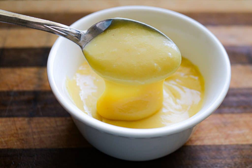 spoon scooping of vanilla pudding out of a white bowl