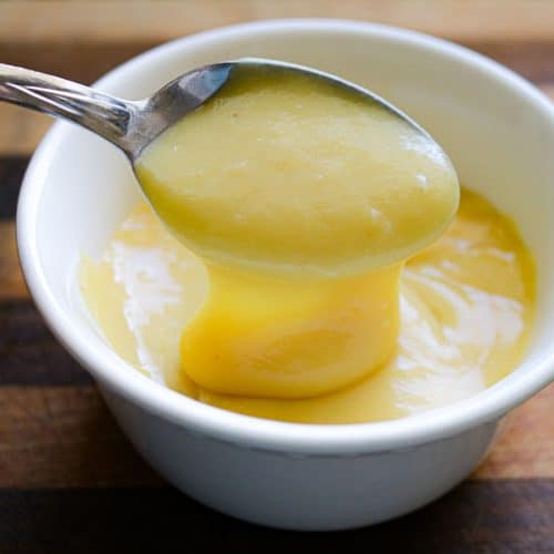 spoon scooping of vanilla pudding out of a white bowl