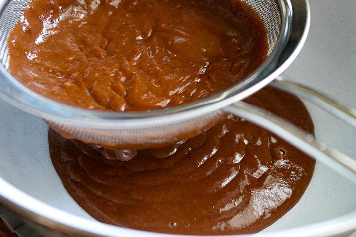 chocolate pudding going through a sieve over a bowl