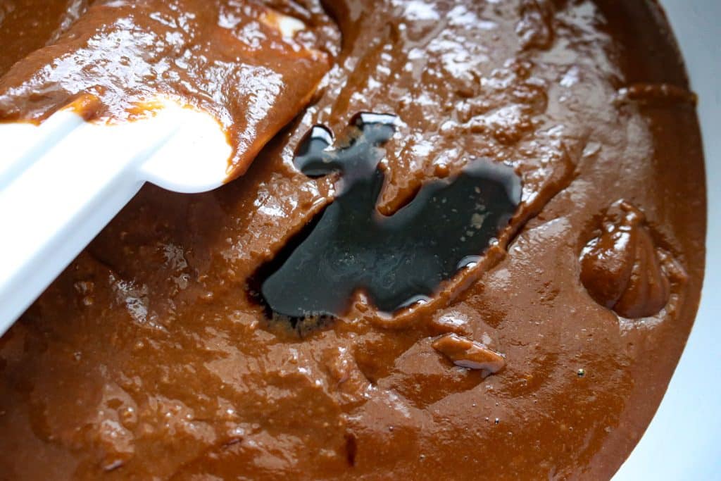 chocolate pudding with a splash of vanilla on top with a white rubber spatula in the bowl