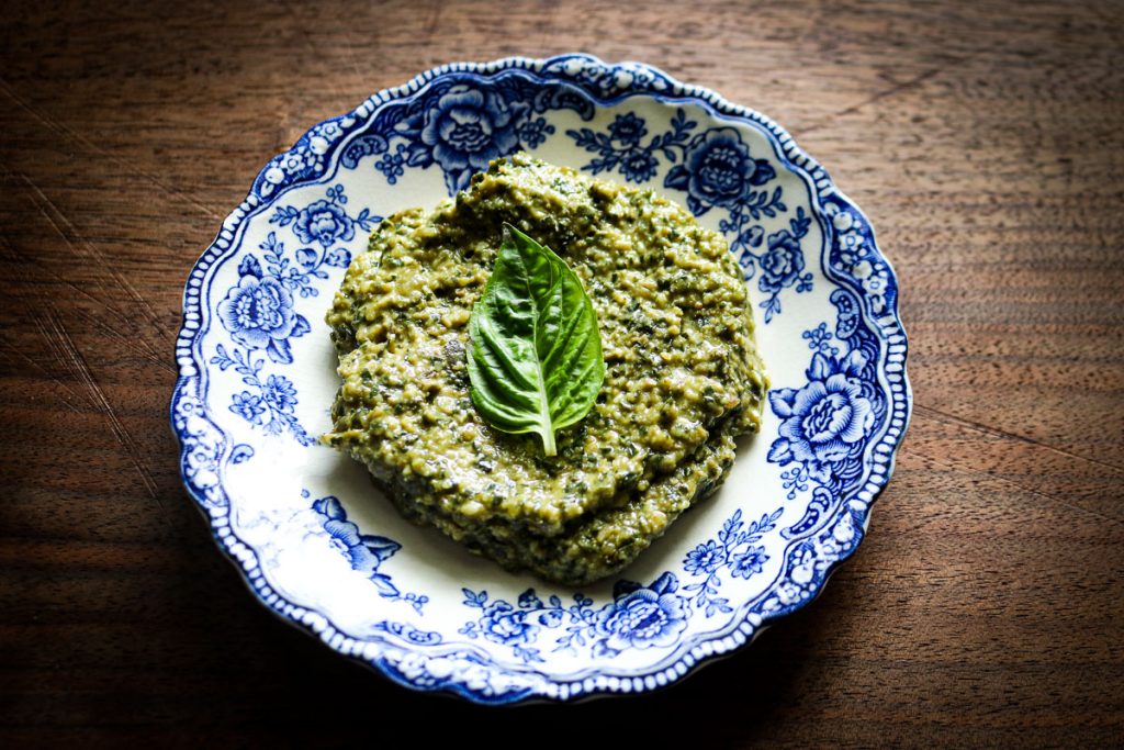 blue and white toile plate with basil pesto and a basil leaf on top of a wooden counter