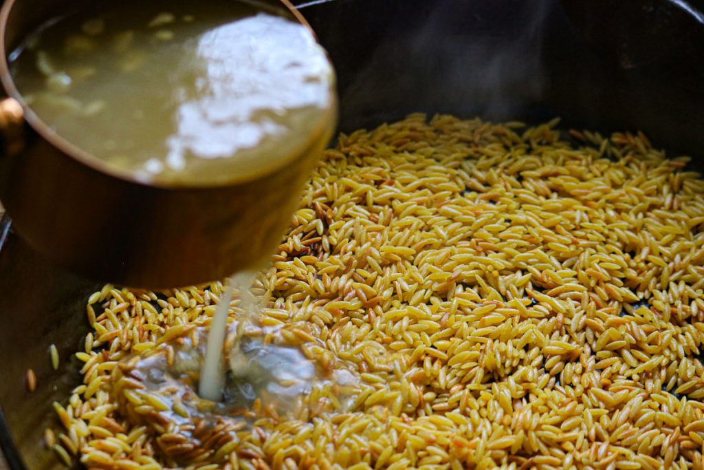 adding chicken broth cream to a skillet of orzo