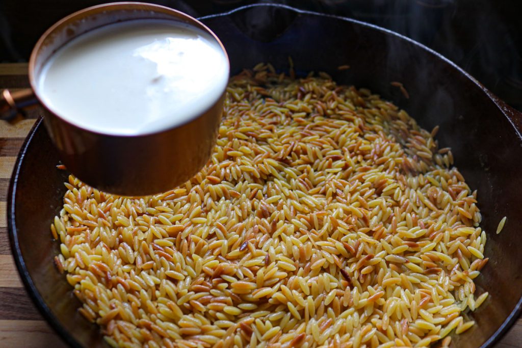 adding heavy whipping cream to a skillet of orzo