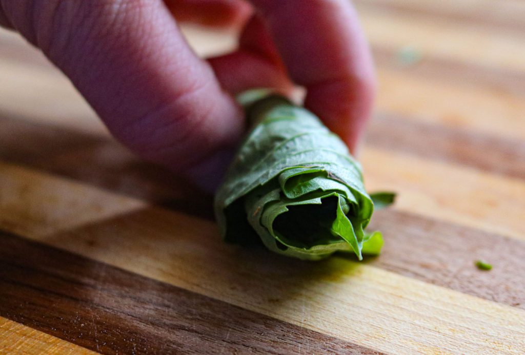 fingers holding rolled up basil leaves on a wooden counter