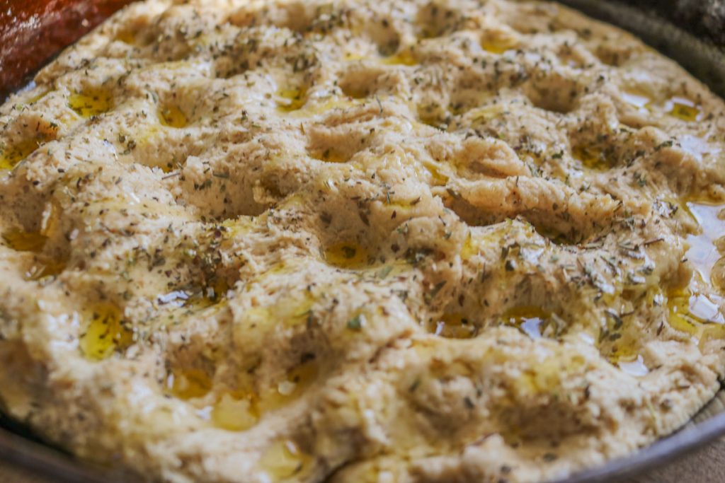dimpled sourdough focaccia in cast iron pan, drizzled with olive oil