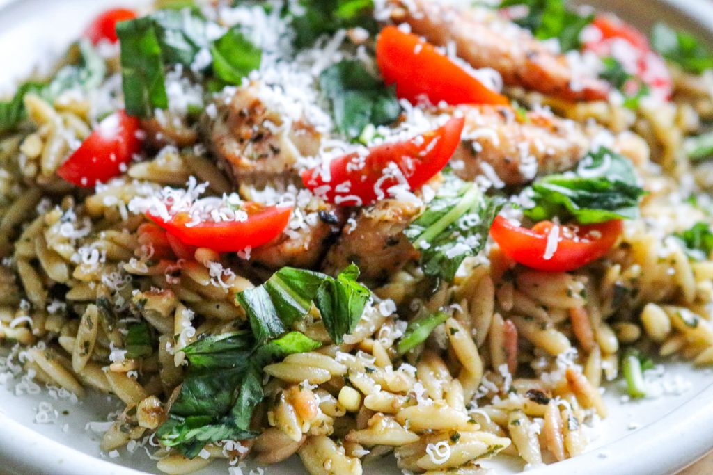 white plate of pesto orzo with chicken and tomatoes