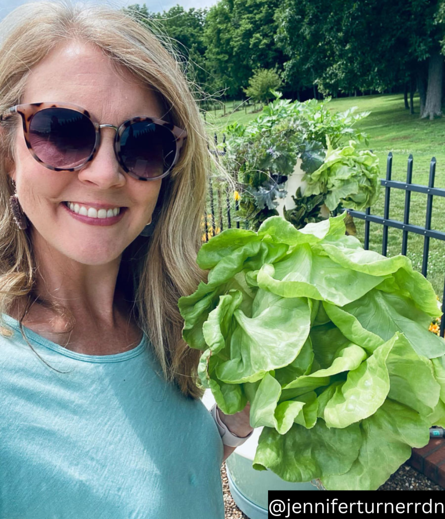 woman holding lettuces in front of juice plus tower garden