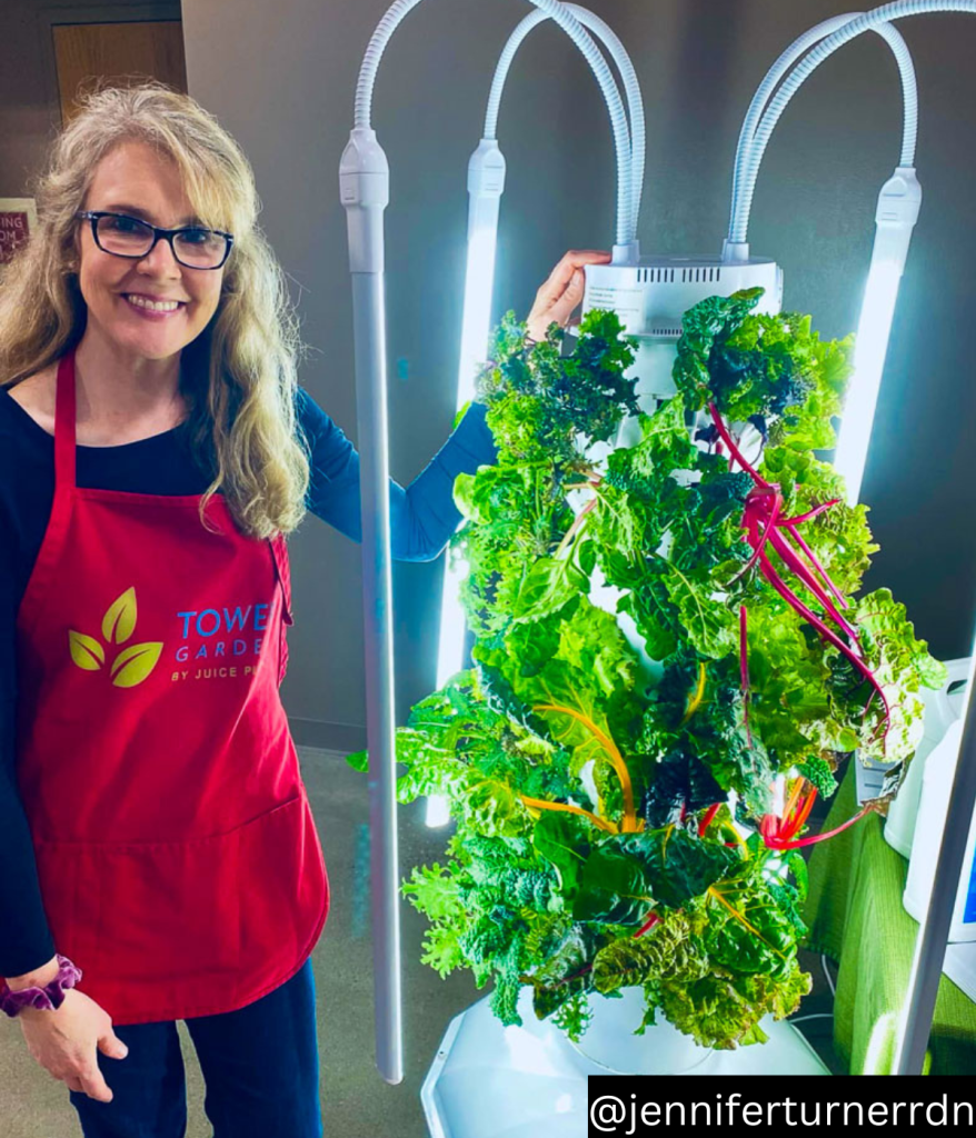 woman standing next to a juice plus tower garden filled with lettuces and greens