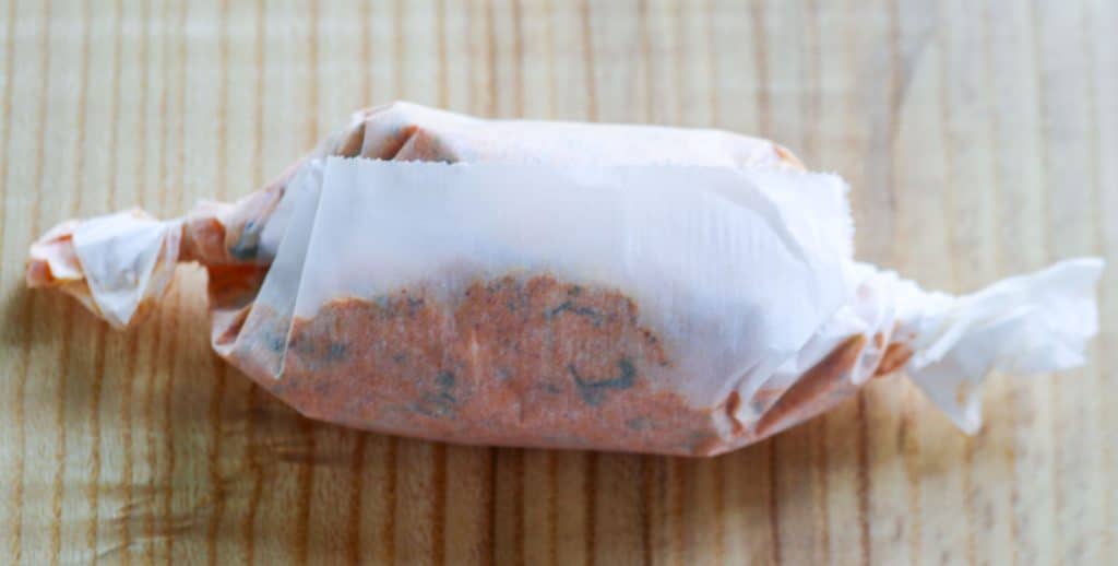 roll of seafood compound butter wrapped in parchment paper on a wooden surface