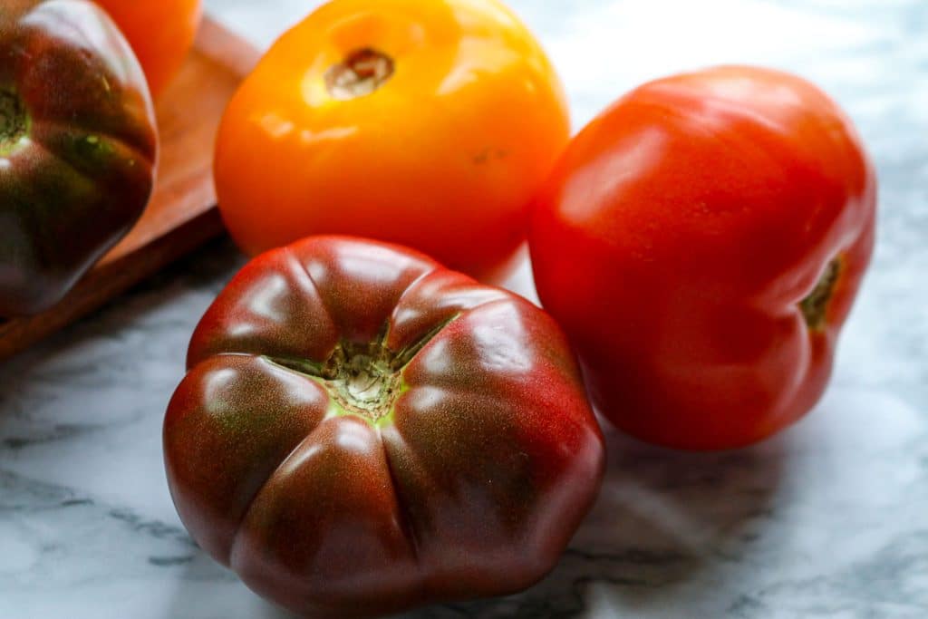 red, purple and yellow tomatoes on marble counter with wooden cutting board