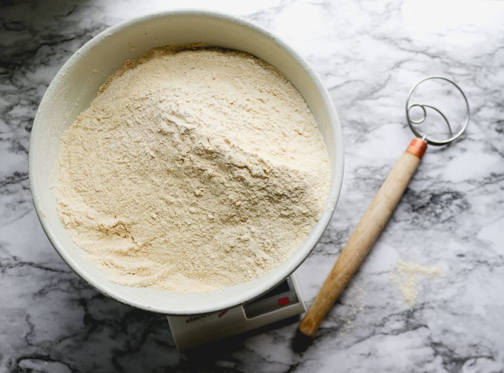 white bowl of flour on a white marble counter with danish whisk